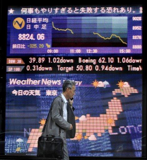 Un hombre pasa junto a un panel electrónico con cotizaciones bursátiles y el tiempo, este martes en Tokio