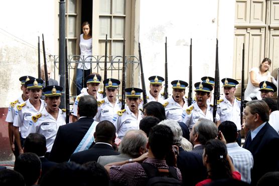 Mientras el primer mandatario tucumano saluda a las fuerzas armadas una vecina curiosa se asoma por una ventana