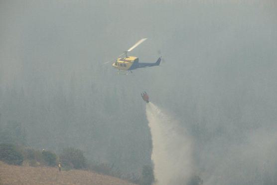 Helicóptero lanza agua entre las llamas