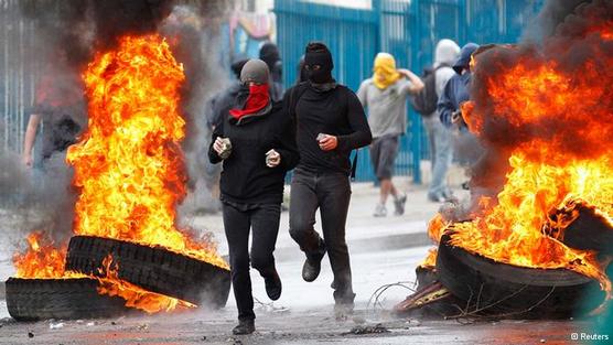 Encapuchados corren en medio de cubiertas incendiadas