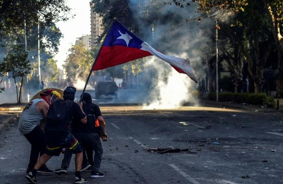 Manifestantes se protegen con un escudo mientras sostienen una bandera de Chile ante la presencia de policías, ayer en Santiago
