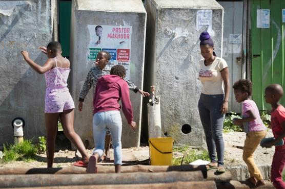 Varias mujeres llenan unos cubos de agua de una fuente junto a unos baños colectivos del 'township' en Ciudad del Cabo