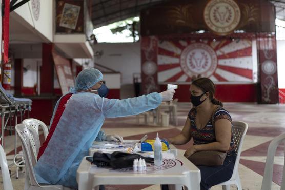 El doctor Wille Baracho le toma la temperatura a una mujer que se sospecha puede tener el coronavirus en el galpón de la escuela