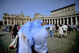 Dos personas se protegen del sol mientras siguen el rezo del ángelus por el papa Francisco en la plaza de San Pedro - AFP